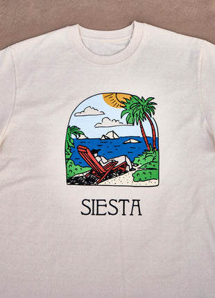 T-shirt Siesta Seaview Unisex Relaxed FitThis T-shirt impresses with its unique design, which depicts a man relaxing on a sun lounger under palm trees against the backdrop of the sea and sun, immersing himself in the Siesta process. Made from 100% organic